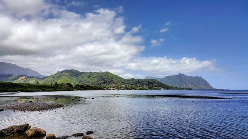 Scenic view of river and mountains against cloudy sky on sunny day