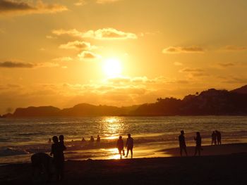 Silhouette people at beach against sky during sunset