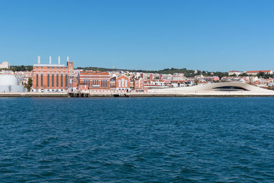 Sea by buildings against clear blue sky