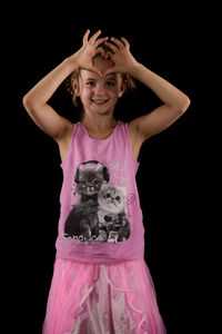 Portrait of cute girl making heart shape on forehead against black background