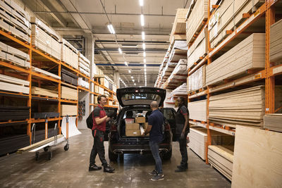 Sales staff communicating with customer standing near car at hardware store