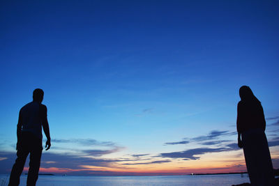 Silhouette couple standing at beach against blue sky during sunset