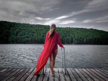 Rear view of woman wearing red dress standing on a wooden pontoon near the lake