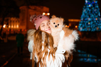 Cute girl holds spitz in her arms in evening on street in light of street