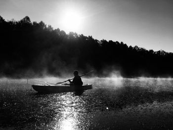 Silhouette man rowing boat against sky