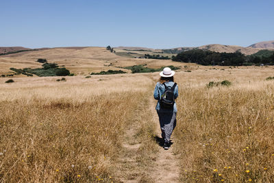 Woman with a backpack walking outdoors through the hills with dry grass, view from the back