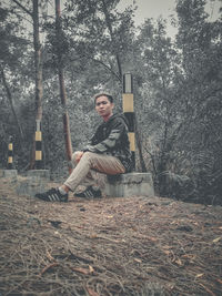 Portrait of young man sitting on plant in forest