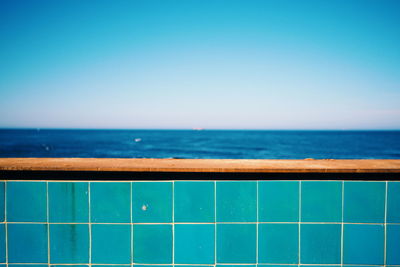 Tiled retaining wall by sea against clear blue sky