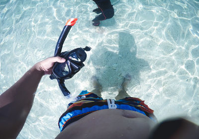 Low section of shirtless man holding snorkel while standing in sea