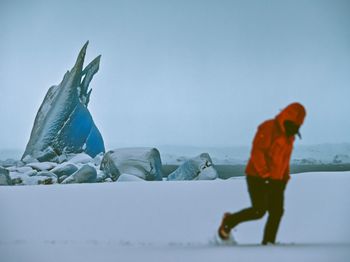 Full length of man walking in snow covered field against sky
