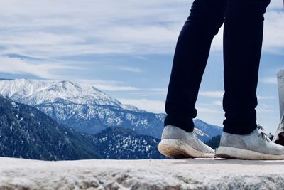 Low section of person standing on land against mountains and sky