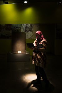 Full length of young woman standing against illuminated light