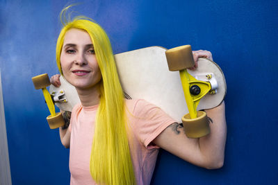 Portrait of young woman holding yellow while standing against blue wall