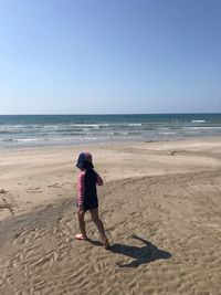 Rear view of woman on beach against clear sky