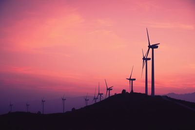 Silhouette wind turbines on land against sky during sunset