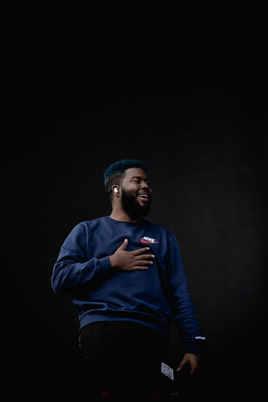 one person, three quarter length, front view, studio shot, young men, standing, black background, young adult, lifestyles, waist up, night, copy space, indoors, casual clothing, men, real people, looking, clothing, cut out, dark, contemplation