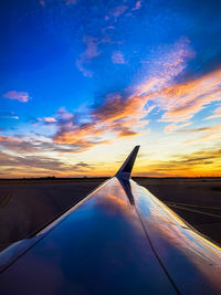 Airplane wing against sky during sunset