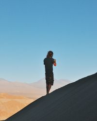 Rear view of person standing on mountain against clear sky