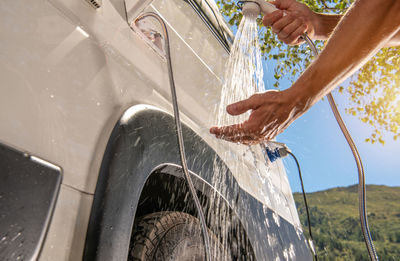 Cropped image of man washing hands by vehicle