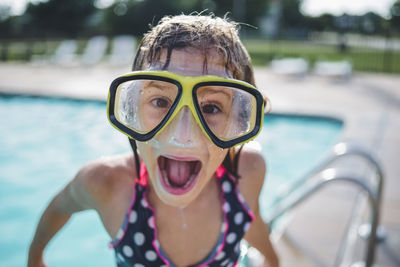 Portrait of girl with mouth open wearing swimming goggles while standing on poolside