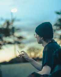 Side view of young man looking away against sky while holding a smoke