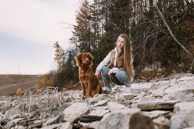 Young woman and dog retriever walks on river shore at autumn season