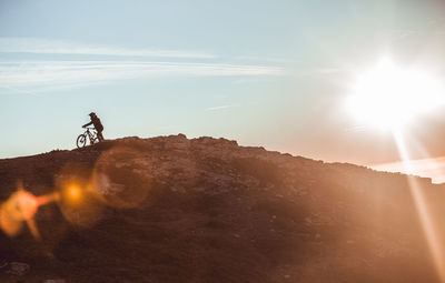 Side view of guy in helmet riding on bicycle on top of mountain with beautiful sunset