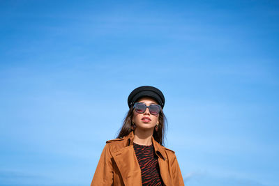 Portrait of young woman standing against blue sky