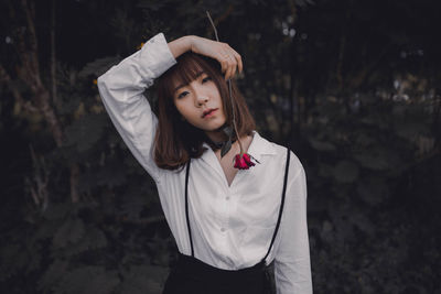 Portrait of woman holding rose flower while standing against trees