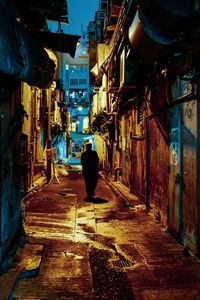 Rear view of man walking on street amidst buildings