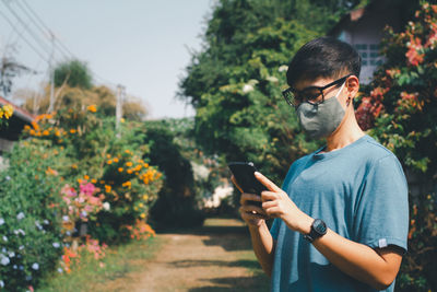 Young man using mobile phone while standing on plants