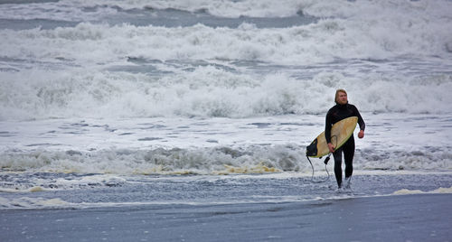 Young man walks with surfboard out of the water in iceland