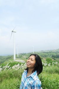 Smiling woman standing on land against windmills and sky