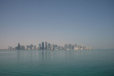 Sea by buildings in city against clear sky