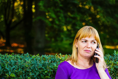 Caucasian blond woman talking, speaking on the phone outside, outdoor. 40s years old woman in purple