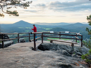 Man on rock shoots photos. traveler with camera takes breathtaking panorama of mountains viewpoint