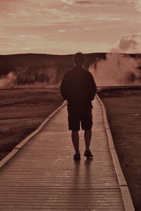 Full length rear view of man walking on boardwalk against hot spring at yellowstone national park