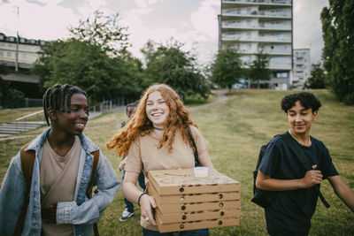Happy teenage girl carrying pizza boxes while walking with friends in park