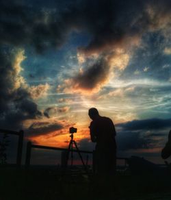 Silhouette man photographing against sky during sunset