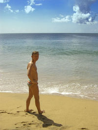 Full length of man in swimming shorts standing on shore at beach during sunny day