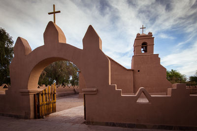 Low angle view of cross amidst buildings against sky