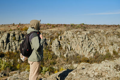 Rear view of man standing on rock against sky