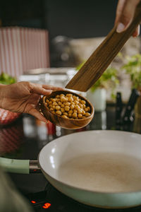 Hands of female chef adding chickpea in cooking pan using wooden spoon at studio kitchen