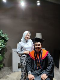 Portrait of smiling woman standing by man wearing graduation gown