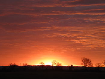 Silhouette trees on field against romantic sky at sunset