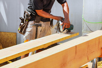 Midsection of man cutting plank during sunny day