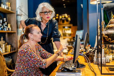 Serious female entrepreneur standing at table and listening to assistant while working on project at computer in expensive house