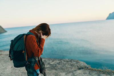 Woman with head in hand standing near sea