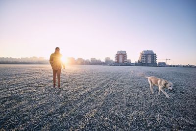 Man with dog standing on field against clear sky during sunset