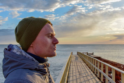 Profile view of young man standing on pier over sea against sky